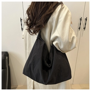 Detailed close-up of a black minimalist nylon shoulder bag worn by a model in a room