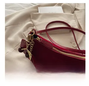 Detail of dark red leather shoulder bag with gold zipper and cherry shaped metal pendant