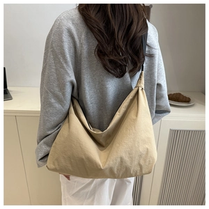 Detail of a large khaki nylon tote bag with adjustable black strap worn by a model