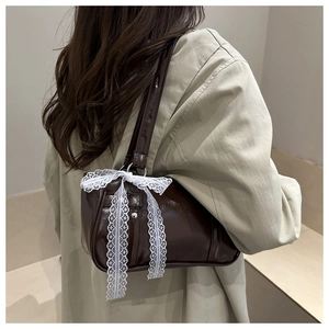 Détail d'un sac à main marron foncé brillant orné d'un grand nœud en dentelle blanche