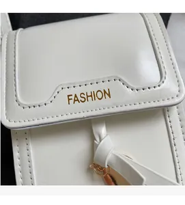 Detail of white PU leather bag with gold FASHION logo and circular metal charm