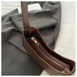 Detail view of smooth golden metal zipper and internal pocket on brown leather crescent bag