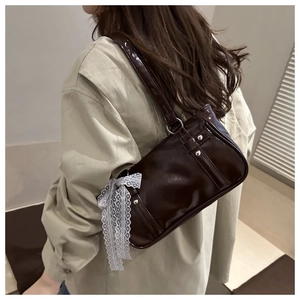 Detail of dark brown glossy underarm bag with a white lace bow charm and silver hardware