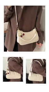 Detail of cream baguette bag featuring cherry charm and elegant metal chain strap