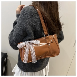 Détail du sac Boston en cuir verni marron avec un grand nœud en dentelle blanche à l'épaule