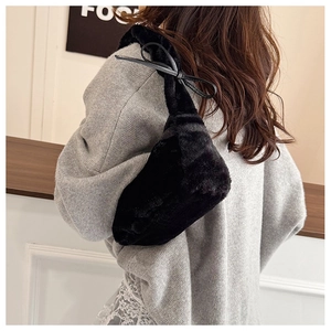 Detail of black plush underarm bag with decorative leather bow on shoulder strap