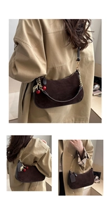 Detail of dark brown suede shoulder bag with gold chain strap and red cherry charm