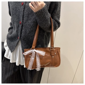 Close-up of brown baguette bag with large white lace bow and silver rivets details