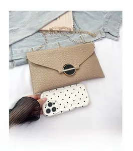 Detail view of woven texture beige clutch with chain strap shown next to a smartphone