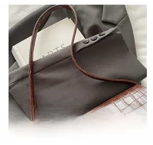 Close-up of brown crocodile pattern leather bag with golden clasp on a grey blazer