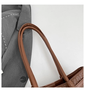Detail of brown woven tote bag featuring leather shoulder strap and fine stitching