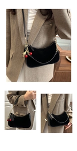 Detail of black suede shoulder bag with gold chain strap and red cherry charm accessory