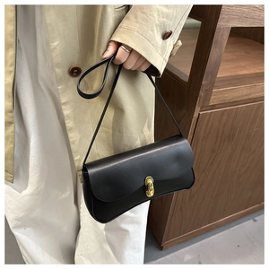 Detail of minimalist black leather baguette bag featuring a sleek gold rectangular clasp