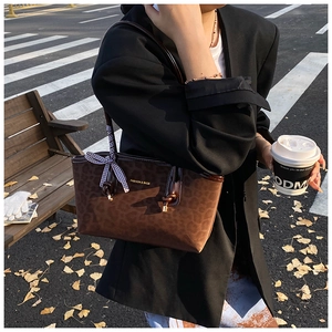 Dettaglio borsa tote leopardata con fiocco a quadri e logo fashion su sfondo autunnale
