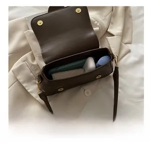 Detail view of small brown crossbody bag capacity showing phone, earbuds and lipstick