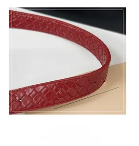 Detail of red faux leather tote bag strap with woven texture and metal buckle holes