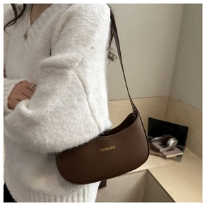 Detail of dark brown matte leather hobo bag with gold lettering shown on a white sweater
