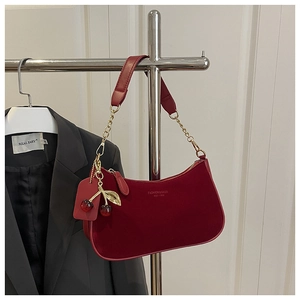 Detail of red suede crescent bag featuring golden chain and cherry charm pendant