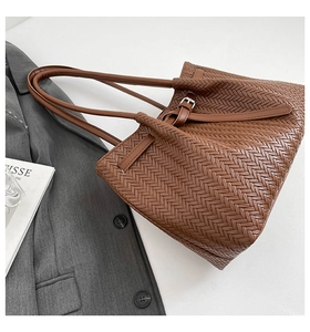 Detail of brown woven tote bag with V-shaped weave pattern and silver buckle on strap