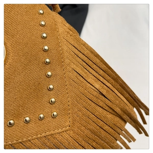Détails des rivets dorés et des longues franges sur un sac besace en daim marron