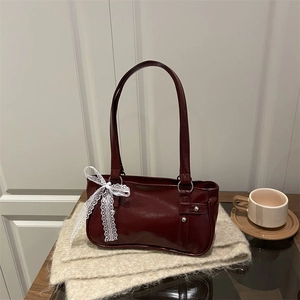 Retro dark red underarm bag with silver studs and a white lace bow on a soft surface