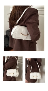 Detail of white crocodile embossed underarm bag with gold curved metal hardware and strap