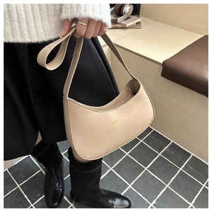 Detail view of beige crescent saddle bag with gold foil branding in a lifestyle setting
