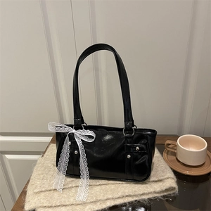 Glossy black shoulder bag with white lace bow and silver rivets on a cozy cafe background