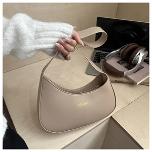 Close-up of beige leather crescent bag with gold logo on a desk with lifestyle items