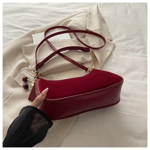 Detail view of red velvet crescent bag with gold chain and cherry pendant decor