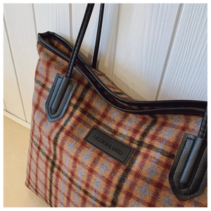 Détail du sac cabas vintage en laine à carreaux avec anses en cuir et logo central chic