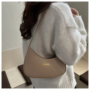 Close-up of a beige half-moon underarm bag with gold lettering on white knit sweater