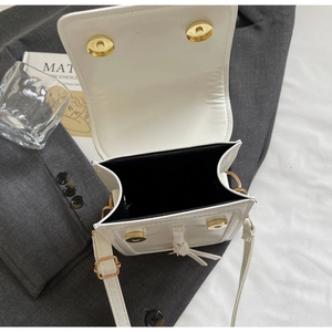 Close-up of a white leather square shoulder bag with gold magnetic snaps and black lining