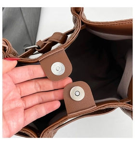 Detail of the silver magnetic closure and pebble leather texture on a brown tote bag