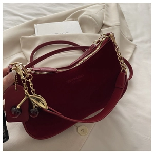 Detail of dark red velvet shoulder bag with gold chain and cherry charm on beige fabric