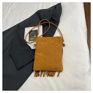 Sac bandoulière en daim fauve avec franges, posé à plat sur un drap blanc chic