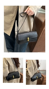 Detail of vintage black crocodile pattern baguette bag with golden clasp and leather strap