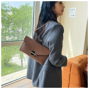Brown woven envelope bag with gold chain strap worn by model in gray blazer