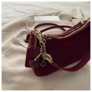 Detail of dark red crescent shoulder bag with golden cherry pendant on white blazer