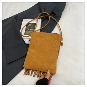 Détail d'un sac besace en daim jaune gingembre avec de longues franges sur fond blanc