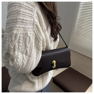 Close-up of retro dark leather underarm bag with gold oval clasp on white sweater