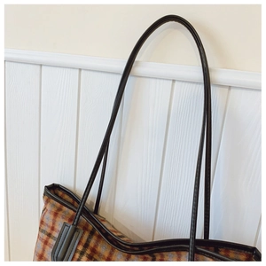 Vue détaillée de la bandoulière en cuir noir et du tissu à carreaux de ce sac