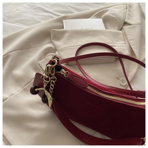 Detail view of burgundy suede shoulder bag with gold cherry charm and fashion logo