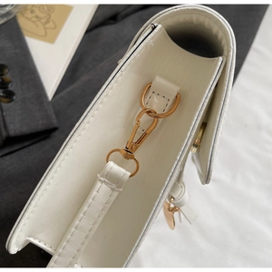 Detailed view of white leather shoulder bag featuring gold metal hook and fine side stitching