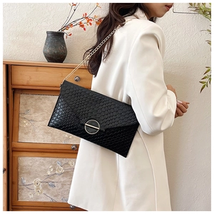 Detail of black woven texture envelope bag with gold ring buckle on model with white blazer
