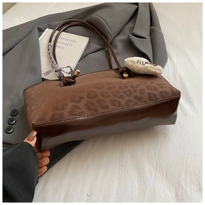 Dettaglio della borsa tote leopardata con ciondolo di peluche e fiocco a scacchi su sfondo grigio