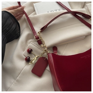 Detail of burgundy shoulder bag featuring suede texture and decorative cherry charm