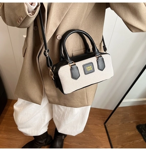 Close-up of beige fabric and black leather Boston bag worn with a khaki suit jacket