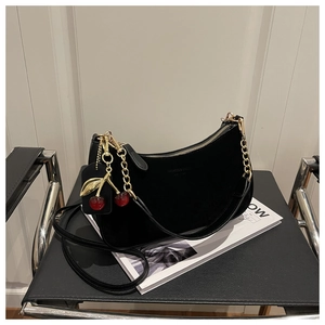 Detail of black crescent hobo bag featuring vibrant red cherry pendants and gold chain