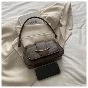 Detail of dark brown faux crocodile leather bag with golden crescent metal trim and phone